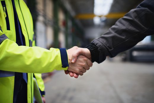 Nahaufnahme eines Händedrucks zwischen Ingenieur und Industriearbeiter in einer Fabrikhalle
